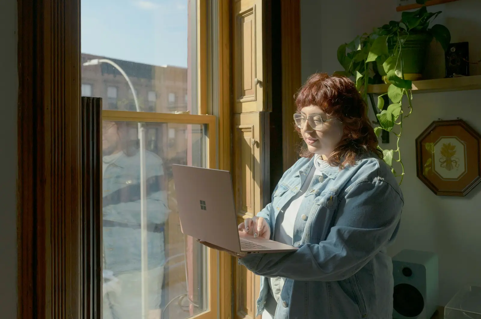 Mulher usando um notebook junto à janela, em um ambiente com plantas.