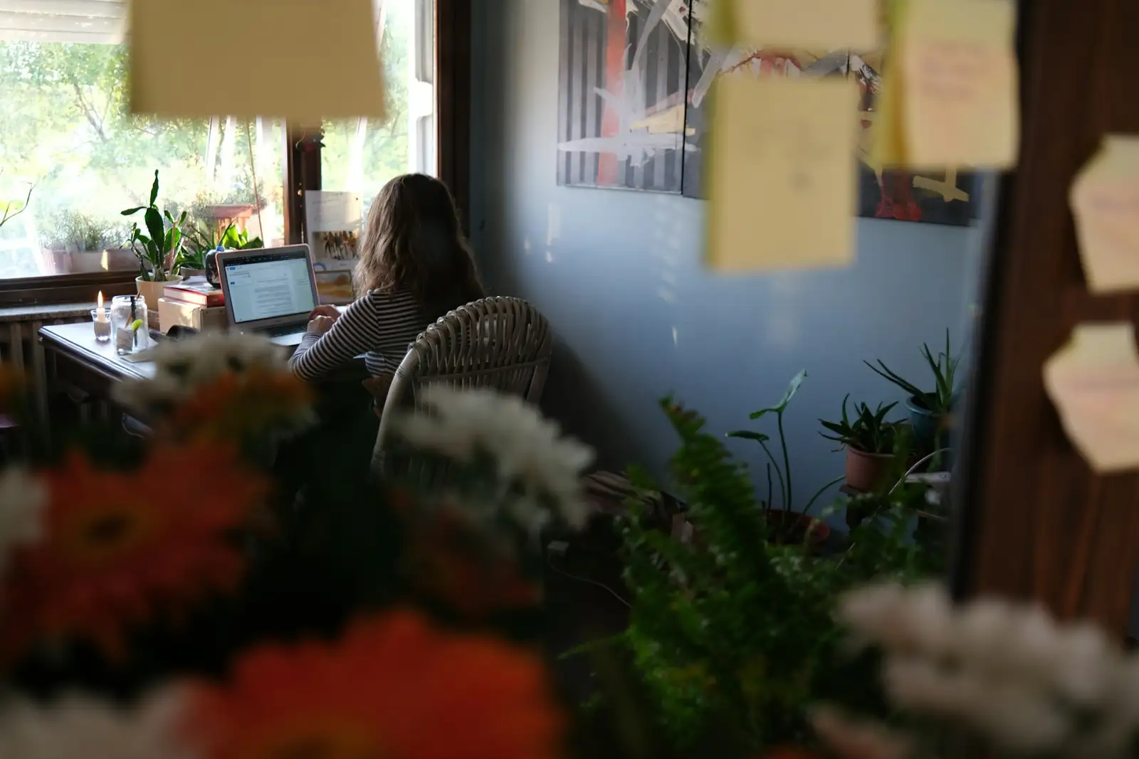 Mulher trabalhando em um notebook em uma sala com plantas.
