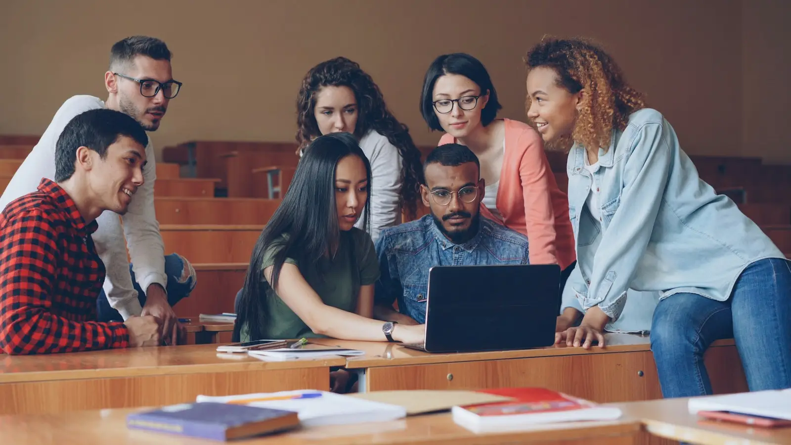 Grupo de estudantes reunidos em volta de um notebook em uma sala de aula.