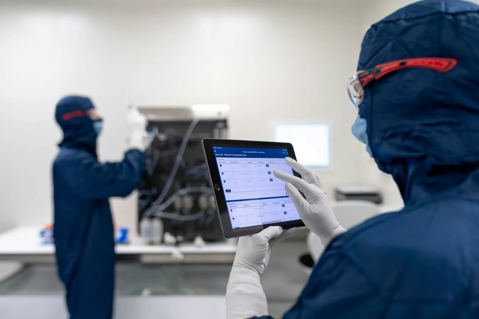 Técnica com roupa de sala limpa consultando um tablet ao lado de um equipamento.