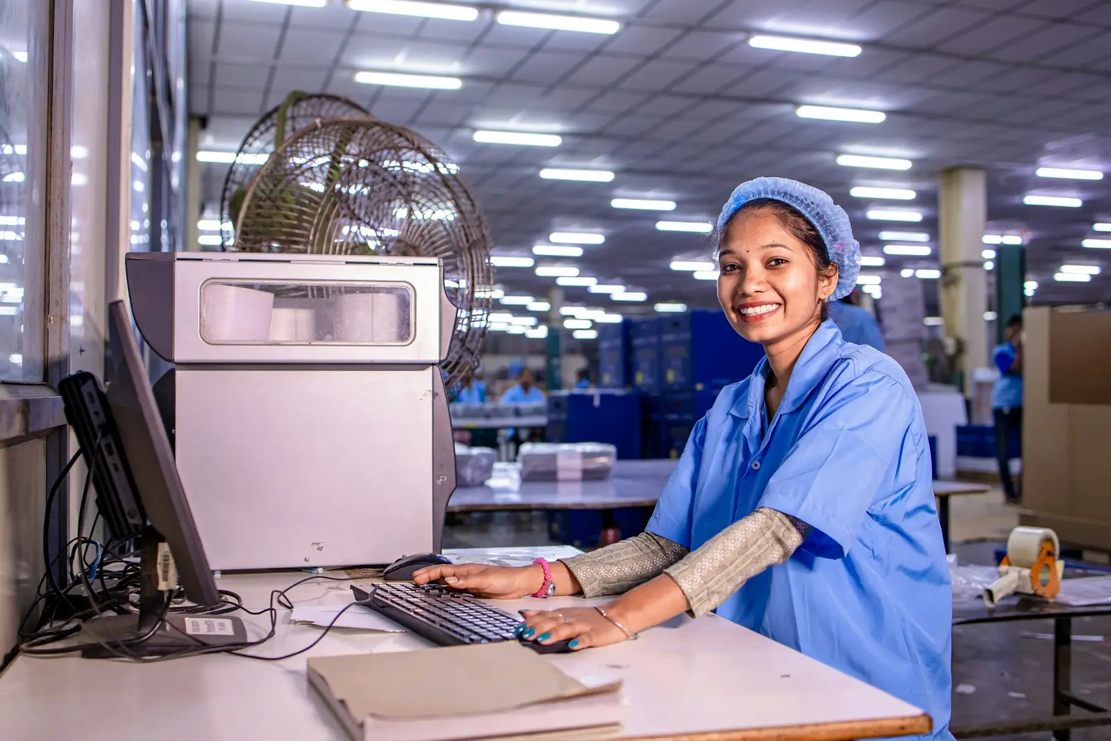 Operadora sorrindo diante de um computador em uma fábrica.