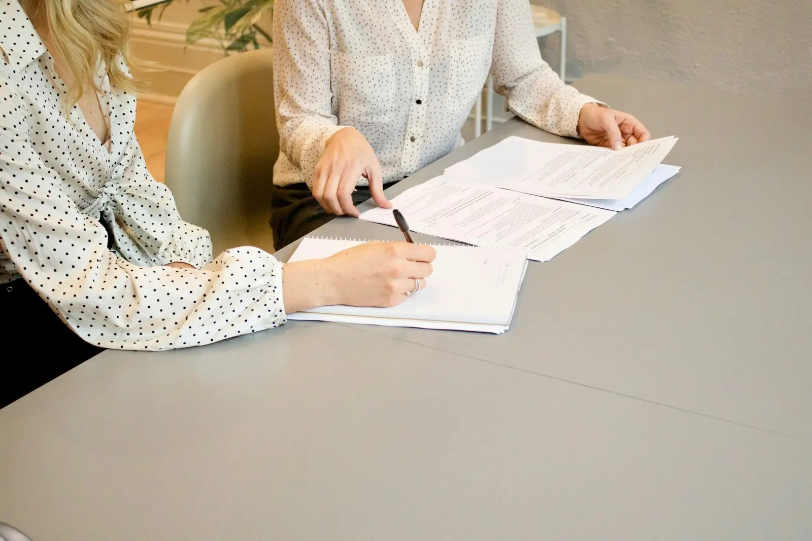 Duas pessoas revisando e assinando documentos sobre uma mesa.