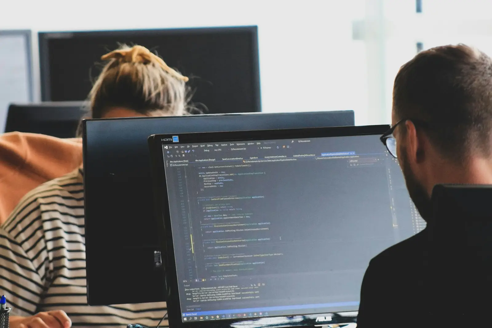 Pessoas trabalhando com código em monitores de um escritório.